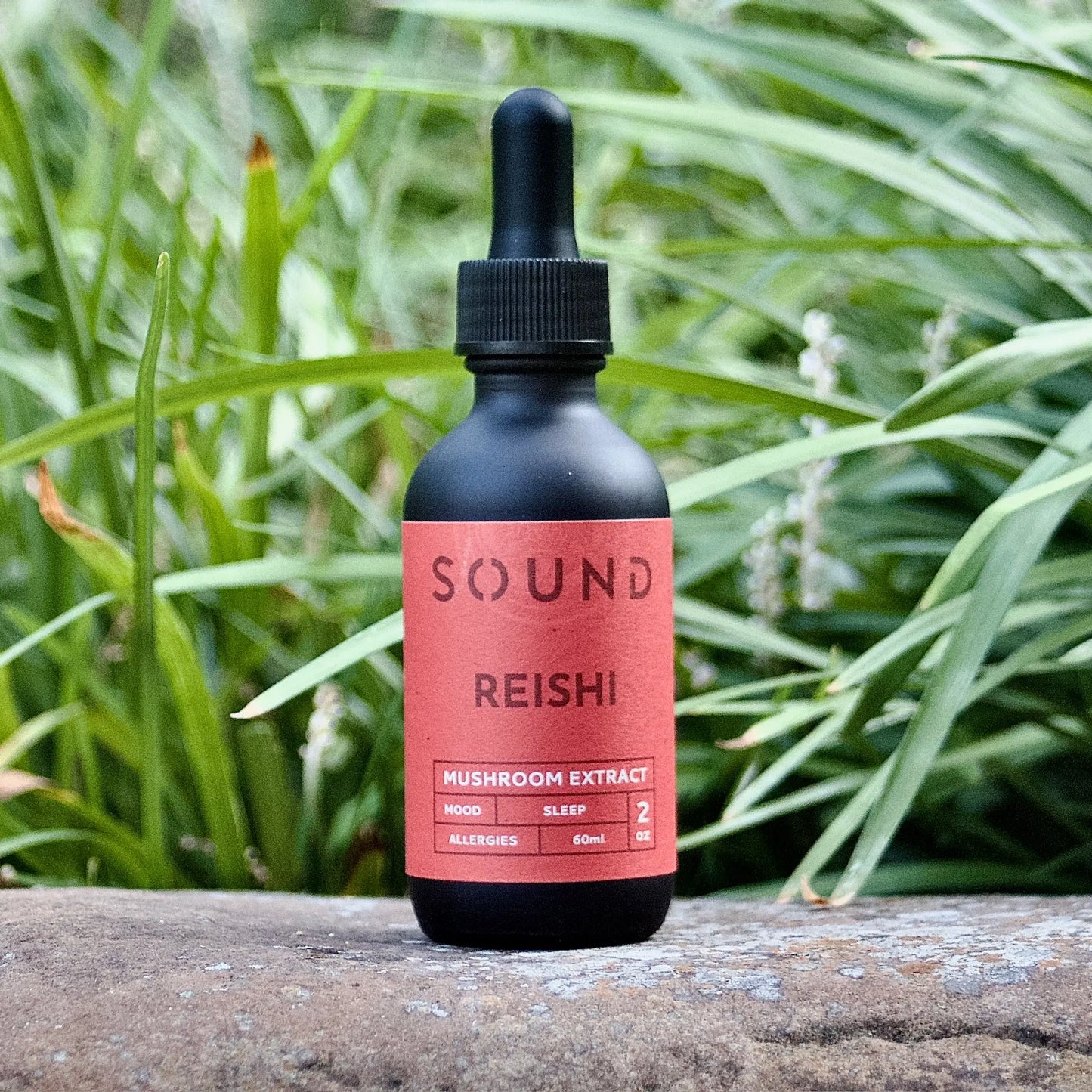 Red Reishi Mushroom Sound Extract 60 ml bottle sitting on rock in front of grass
