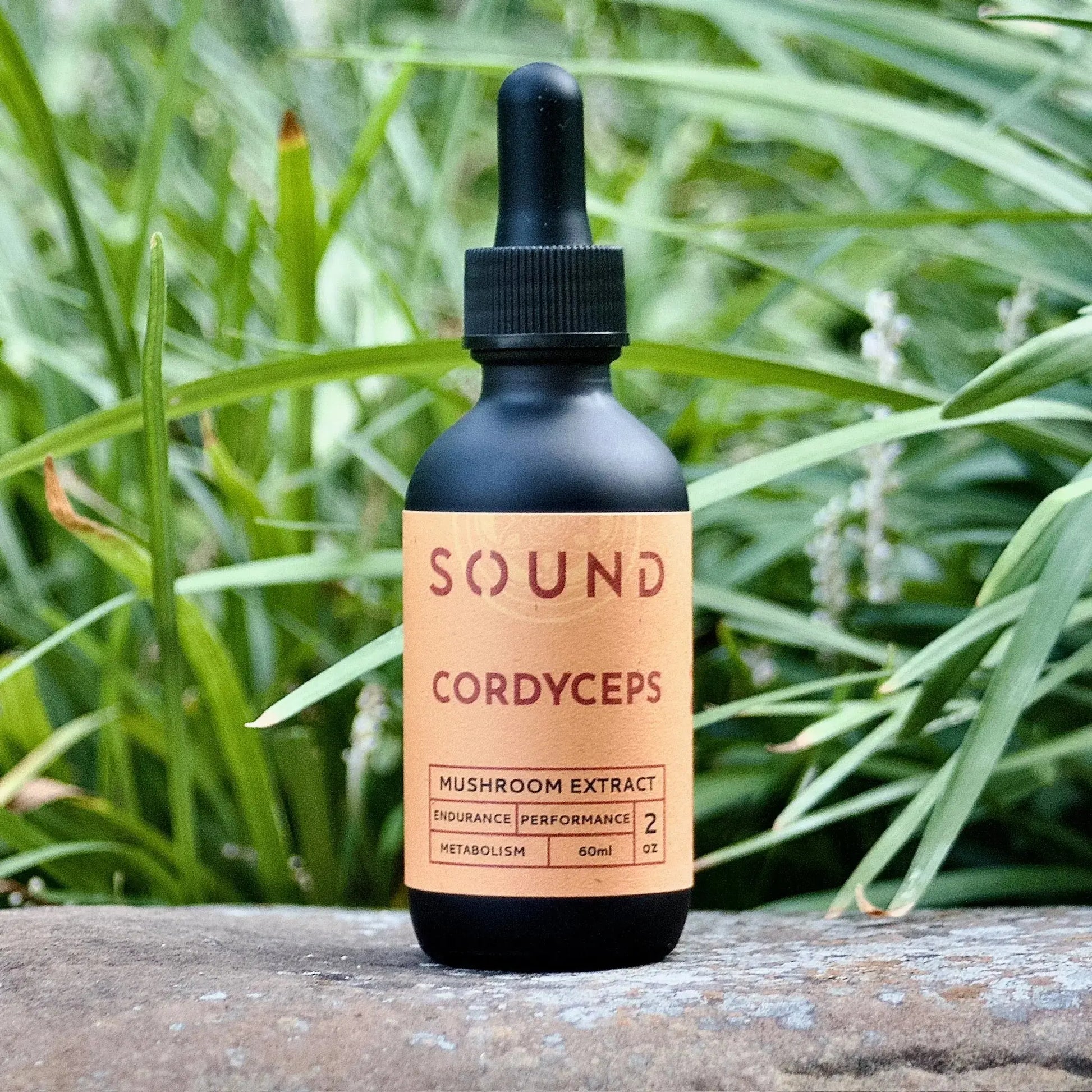 Orange Cordyceps Mushroom Sound Extract 60 ml dropper bottle sitting on rock in front of grass